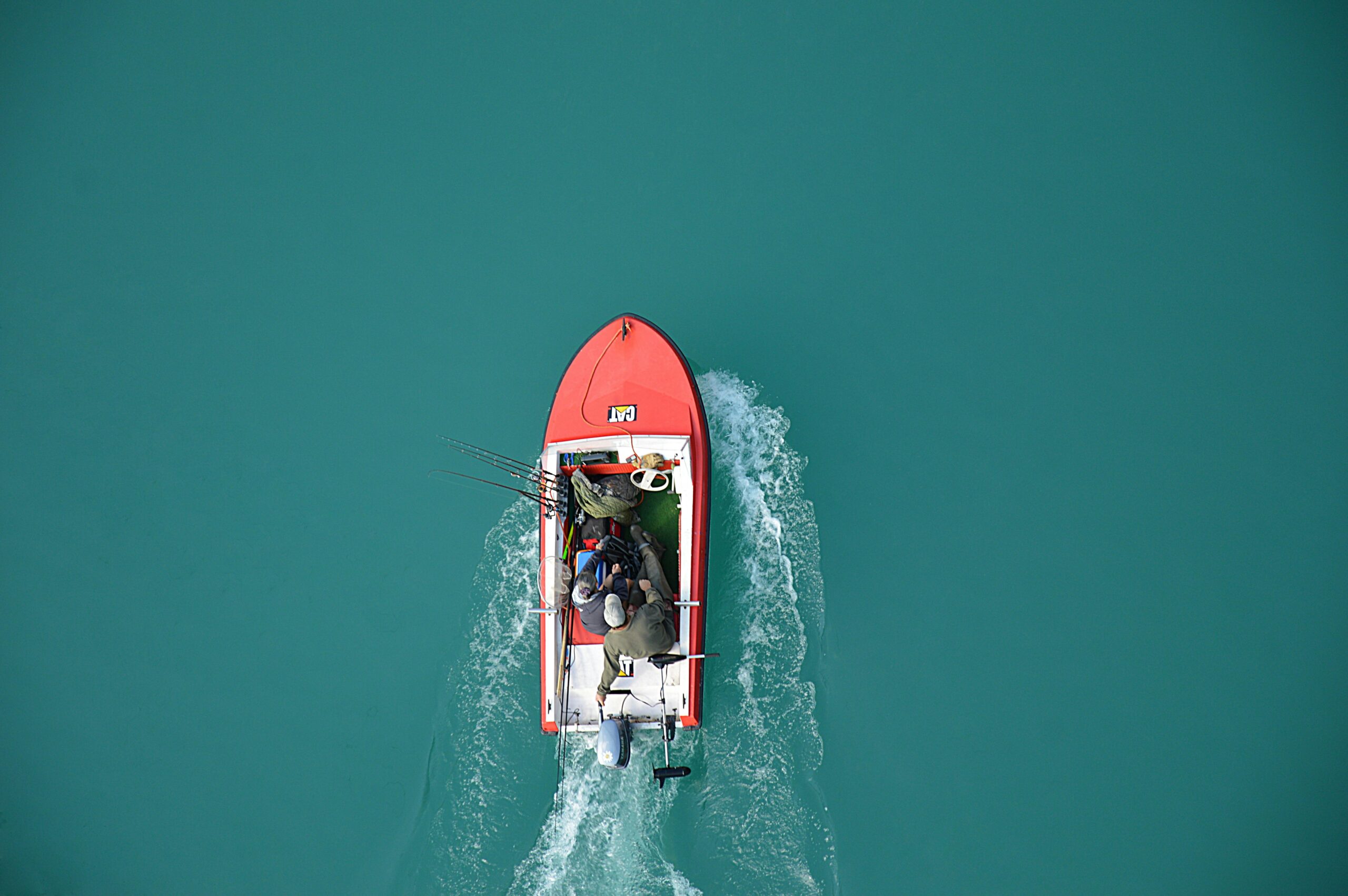 Home Top view of a red motorboat with fishermen navigating open turquoise waters.